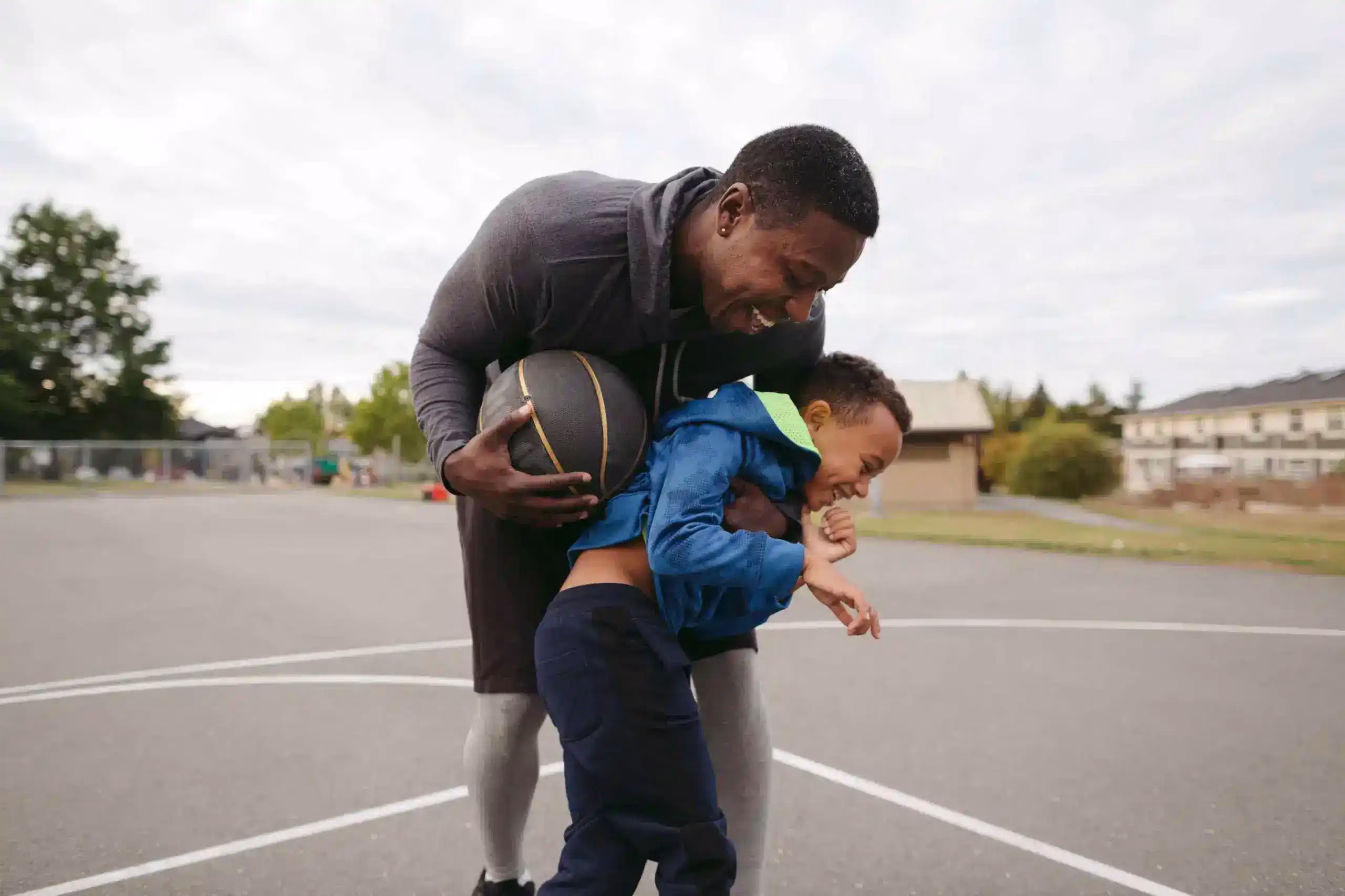 A man and his child laughing on the basketball court