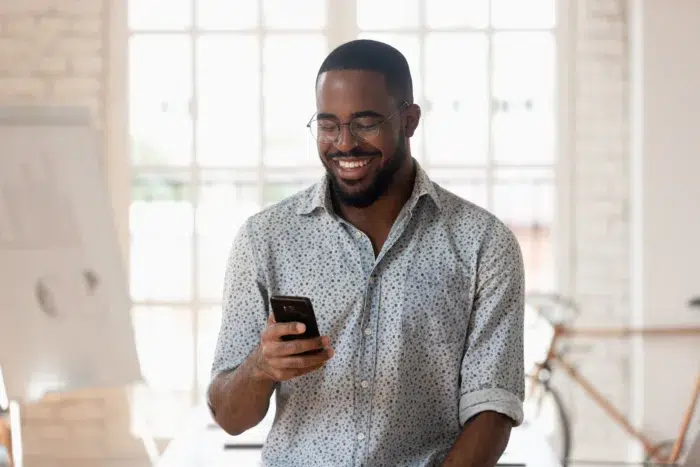 Happy businessman holding smartphone s standing in office - Community Choice Credit Union