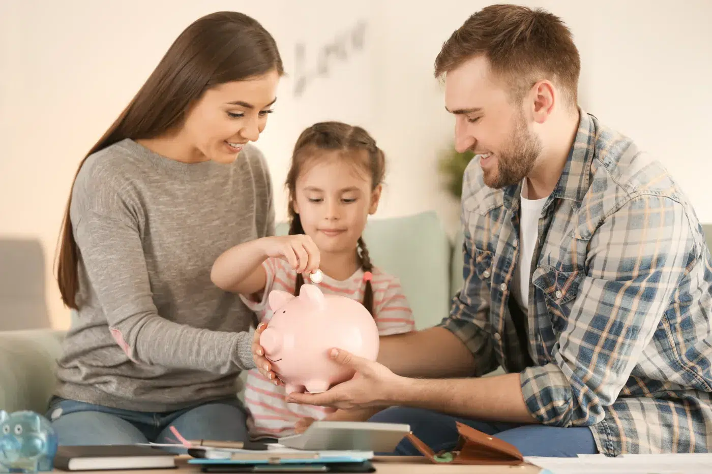 A mom and dad help their daughter put money in a piggy bank.