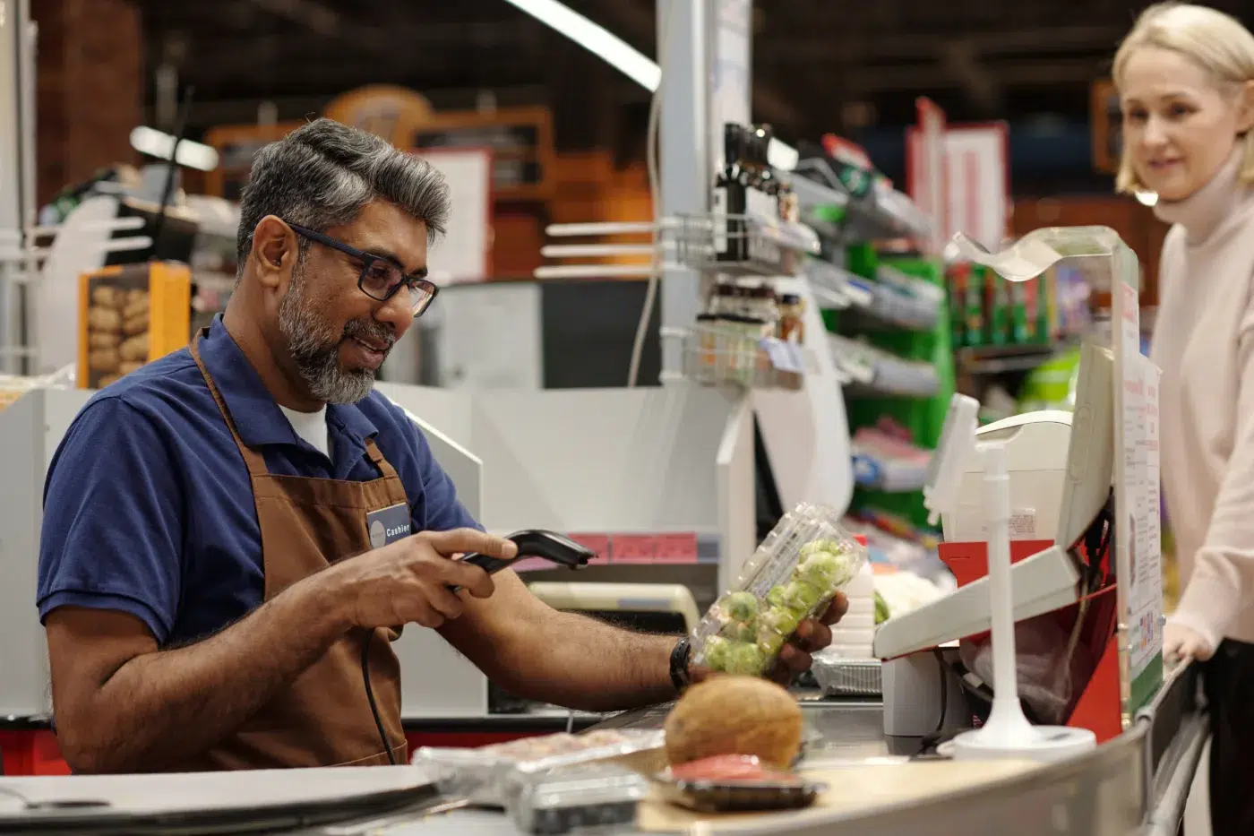 Side view portrait of smiling man scanning items while working at supermarket checkout station, Community Choice Credit Union