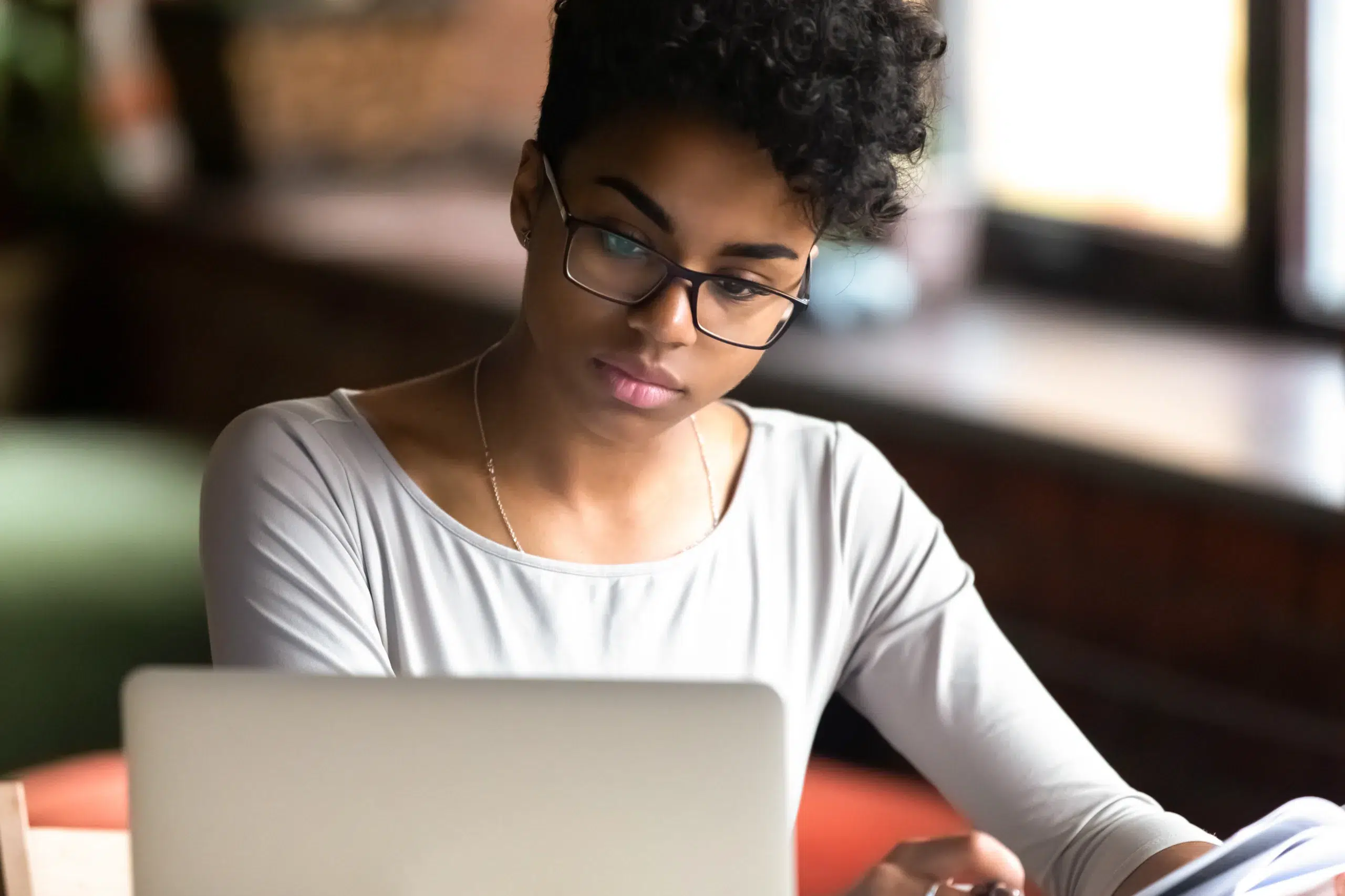 Thoughtful millennial woman in glasses looks at laptop screen. Community Choice Credit Union in Michigan.