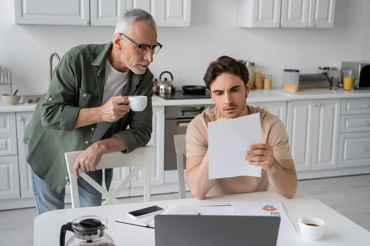 serious young man looking at document near laptop and senior dad with coffee cup - Community Choice Credit Union