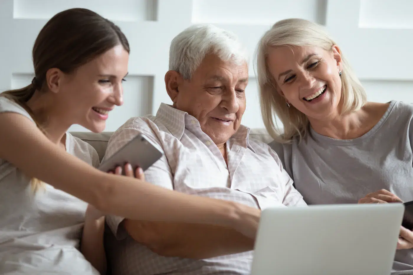 Estate planning with Community Choice Credit Union. Smiling mature parents sit relax on couch with grownup daughter using modern laptop gadget together, happy senior mom and dad rest have fun watch video with adult millennial girl on computer
