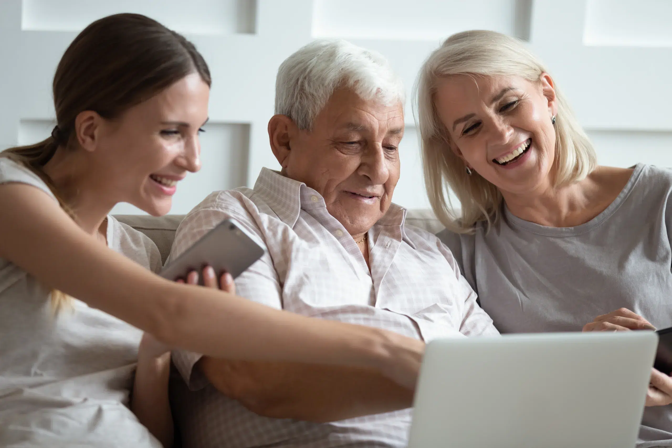Estate planning with Community Choice Credit Union. Smiling mature parents sit relax on couch with grownup daughter using modern laptop gadget together, happy senior mom and dad rest have fun watch video with adult millennial girl on computer